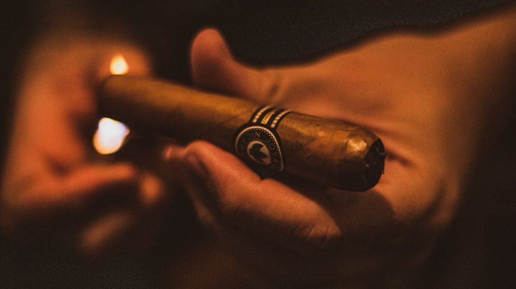 A detailed close-up shot of a hand lighting a cigar in a dark setting.