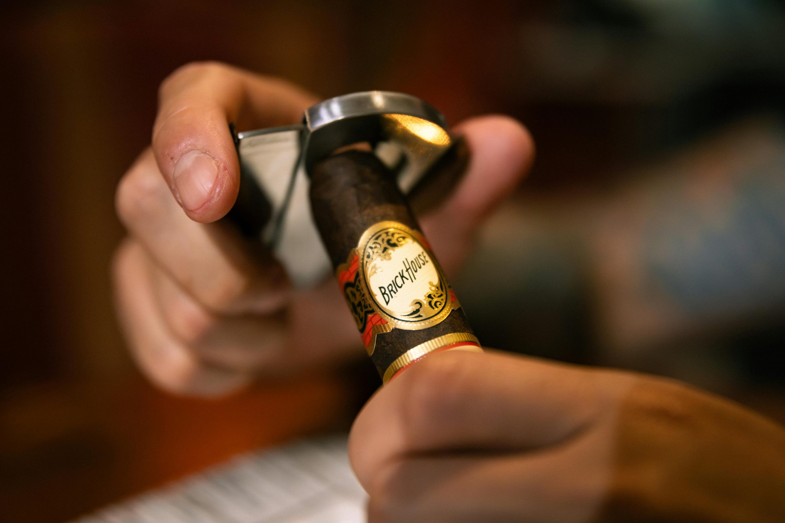 Focused image of a person using a cigar cutter on a premium cigar indoors.